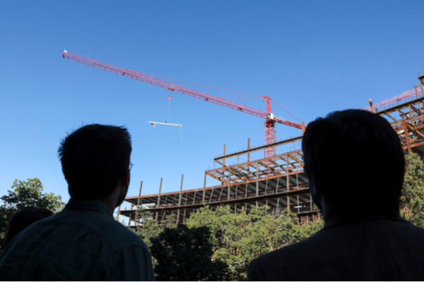 Guests looking as a crane takes a beam, signed by university faculty and staff, and places it on the Rankin Health Education Building.