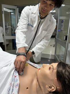 Student using stethoscope to listen for heart sounds on a simulator. 